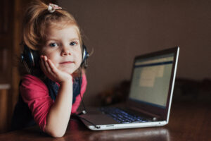 little girl with headphones listening to music, using laptop